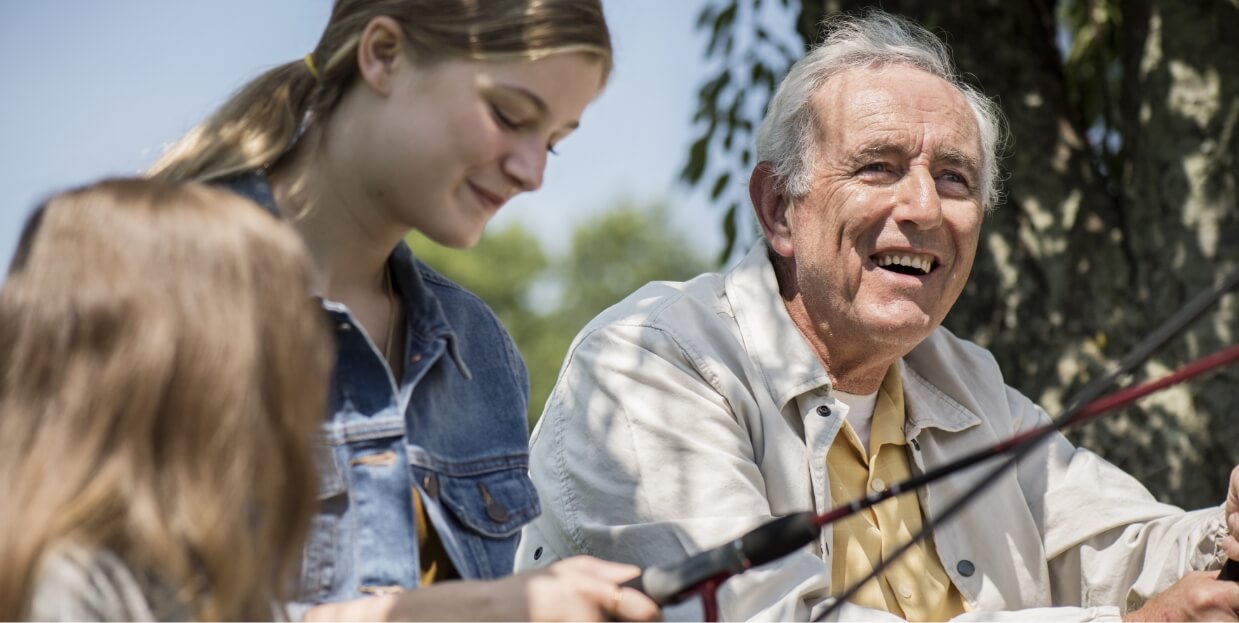 Smiling male in his 60s fishing outdoors with two adolescent girls.